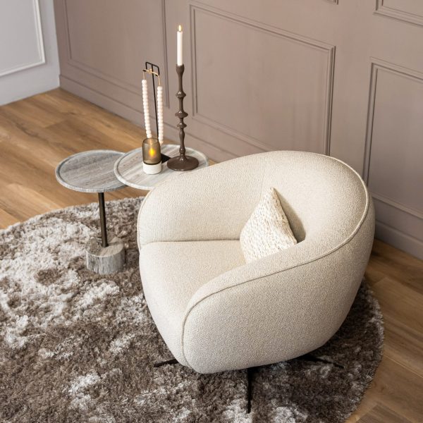 Top view of the Lio armchair in cream bouclé upholstery, placed on a soft textured rug beside marble side tables in a warm contemporary interior.